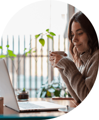 a woman holding a cup of coffee looking at a laptop