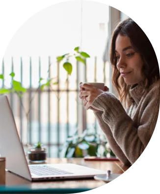 a woman holding a cup of coffee looking at a laptop